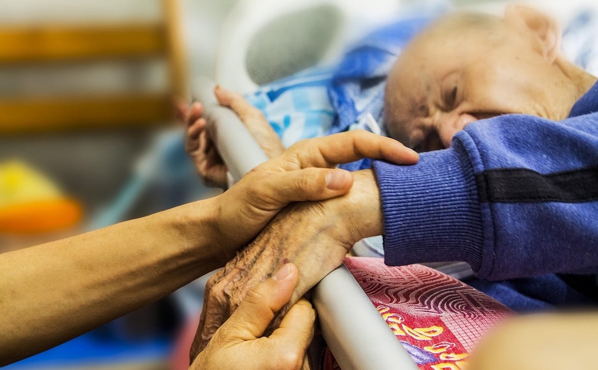 Hands holding the hand of an elderly man lying in bed